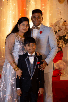 a man and woman pose with a boy in a tuxedo on a red carpet