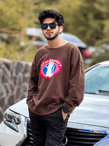 a man wearing sunglasses stands in front of a car with a sweatshirt that says " let's project "