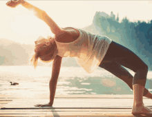 a woman is doing a yoga pose on a dock near the water