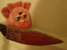 a pink furby stuffed animal is holding a bloody knife in its mouth .