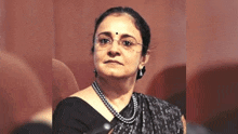 a woman wearing glasses and a pearl necklace is sitting in a chair looking at the camera .