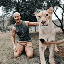 a man kneeling next to a lion wearing a grey tank top that says ' tribe tribe tribe ' on it