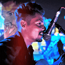 a man singing into a microphone with a reflection of another man in the background