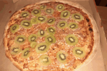 a pizza with kiwi slices on it is in a box