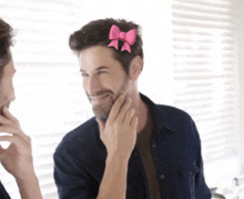 a man with a pink bow in his hair looks at himself in the mirror