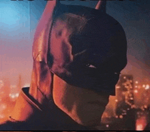 a close up of a person wearing a batman mask with a city in the background