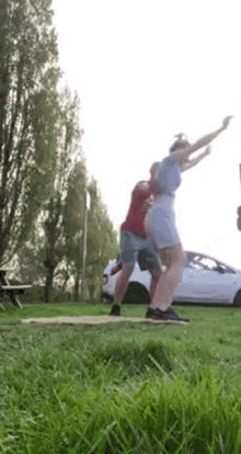 a man and a woman are jumping in the air in a field with a car in the background .