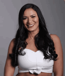 a woman with long black hair is smiling and wearing a white crop top