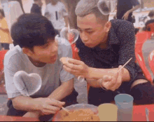 two young men are sitting at a table eating food with chopsticks and a heart shaped soap bubble in the background