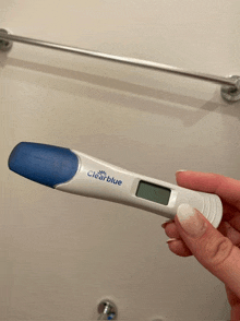 a woman is holding a clear blue pregnancy test