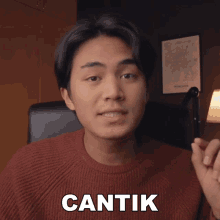 a man wearing a red sweater says cantik in white letters