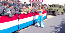 a woman in a blue and white outfit stands in front of a crowd of soldiers and a military vehicle