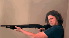 a man with long hair is holding a shotgun and making a funny face .