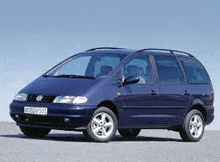 a blue volkswagen sharan minivan is parked on the side of a road .