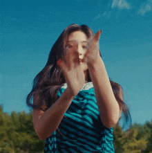 a woman in a blue and white striped dress is making a peace sign with her hands in front of a blue sky .