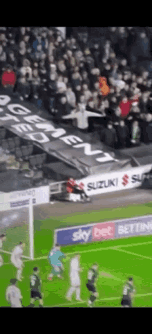 a soccer game is being played on a field with a banner that says ' suzuki ' on it .