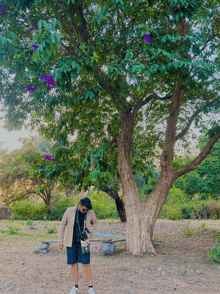 a man stands under a tree with purple flowers