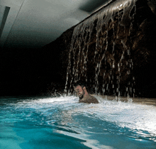 a man in a pool with a waterfall behind him