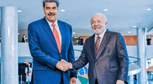 two men in suits shaking hands in front of a brazilian flag