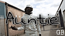 a man wearing a mask and a hat is standing in front of a fence with the word auntie on it