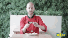 a man in a chef 's uniform is sitting at a table with a plate of food and an ikea logo in the background