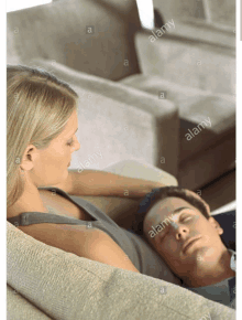 a woman sits on a couch next to a man sleeping