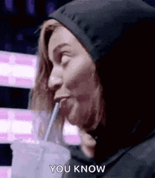 a woman in a hoodie is drinking through a straw .