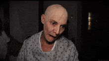 a woman in a hospital gown with a bald head is looking at the camera .