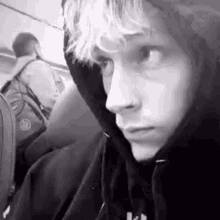 a black and white photo of a young man wearing a hoodie on a bus .