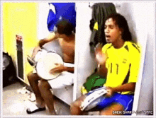 a man in a yellow shirt with the number 11 on it sits in a locker room