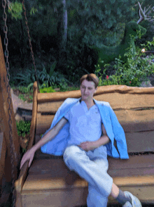 a man in a blue jacket is sitting on a wooden swing