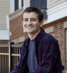 a man in a plaid shirt is smiling in front of a brick building .