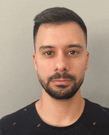 a man with a beard and a black shirt looks at the camera