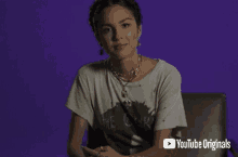 a woman is sitting in a chair in front of a purple background wearing a t-shirt and a necklace .