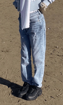 a person standing on a sandy beach wearing blue jeans and black shoes