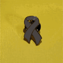 a pin with a gray ribbon on a yellow surface