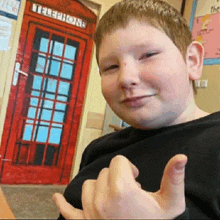 a boy is giving a thumbs up in front of a red telephone booth