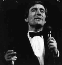 a man in a tuxedo is singing into a microphone on stage .