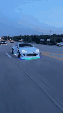 a white car is driving down a highway with a rainbow of lights on the tires .