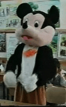 a stuffed mickey mouse mascot is standing in a classroom .