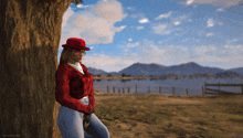 a woman leaning against a tree with mountains in the background