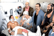 a group of men standing around a man in a hospital bed with a guitar