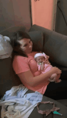 a woman in a pink shirt holds a baby on a couch