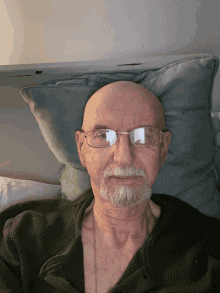 a bald man with glasses laying on a bed