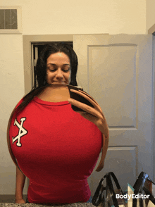 a woman is taking a selfie in front of a mirror while wearing a red shirt with a white x on it