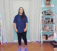 a girl in a blue shirt and black leggings is standing in front of a shelf with toys on it