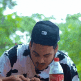 a man wearing a black hat and a cow print shirt is eating a hamburger next to a bottle of coca cola