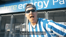 a man wearing sunglasses and a blue and white striped shirt stands in front of a sign that says nature energy park