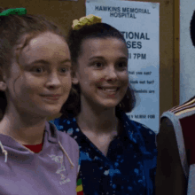 two girls smile in front of a hawkins memorial hospital sign