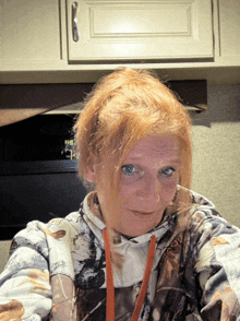 a woman wearing a camo sweatshirt looks at the camera while standing in front of a stove